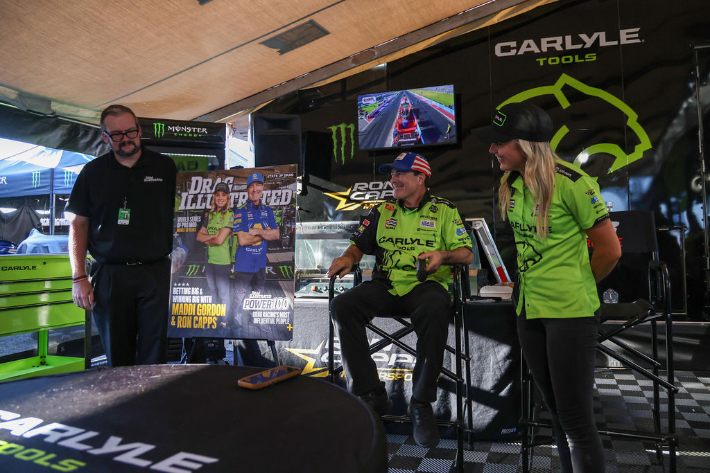 Ron Capps and Maddi Gordon in the Carlyle Tools hauler beside the Drag Illustrated Power 100 cover at the 2026 NHRA U.S. Nationals