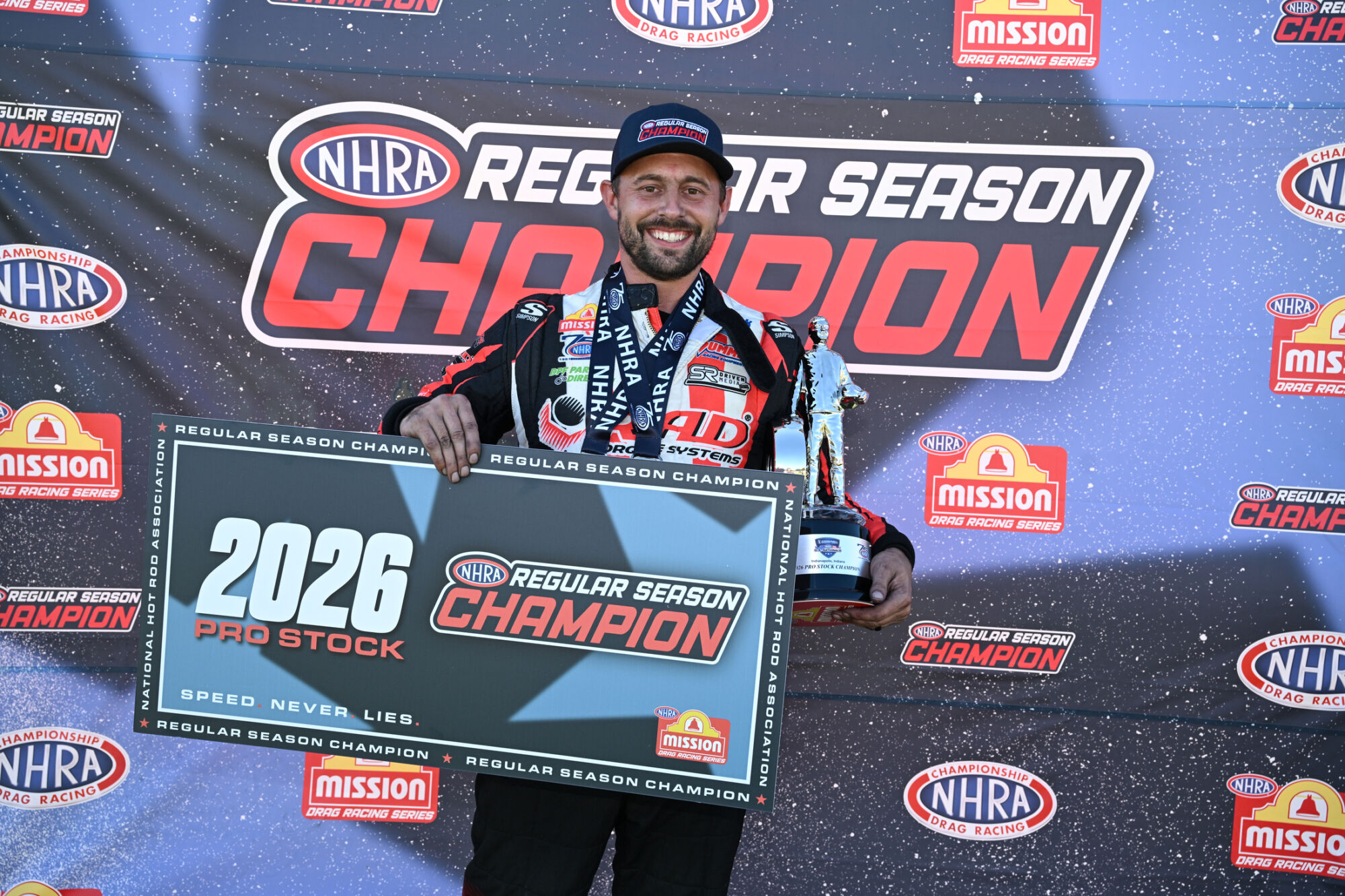 Dallas Glenn holds the 2026 NHRA Pro Stock Regular Season Champion sign and trophy at Lucas Oil Indianapolis Raceway Park