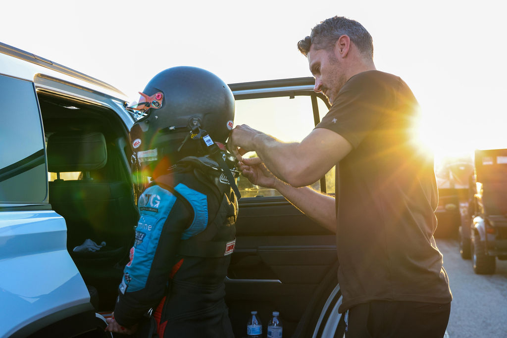 A driver is helped into a helmet at sunset in the pits at the 2026 NHRA U.S. Nationals