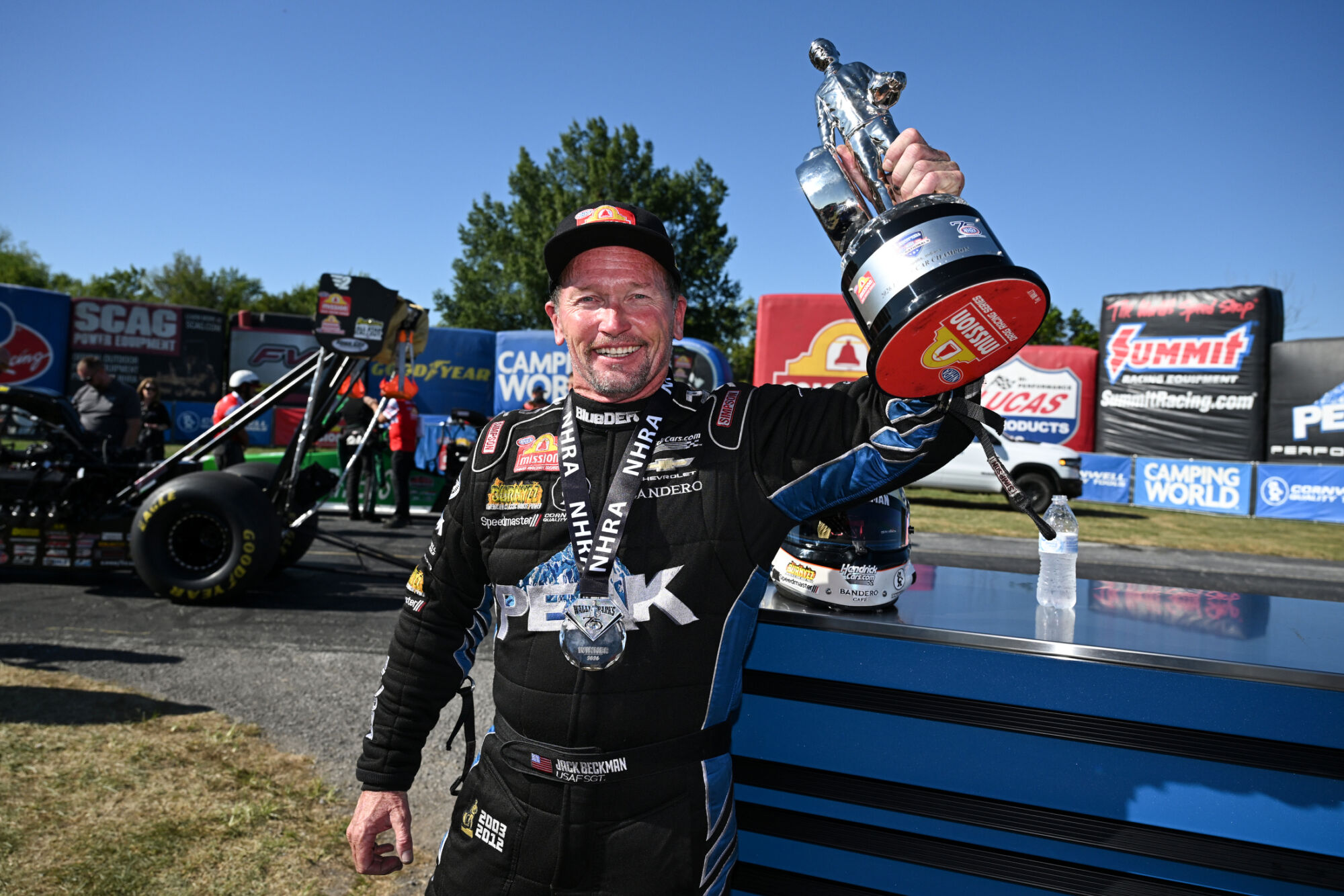 Jack Beckman raises the Wally trophy beside the PEAK Chevrolet Funny Car at the 2026 NHRA U.S. Nationals