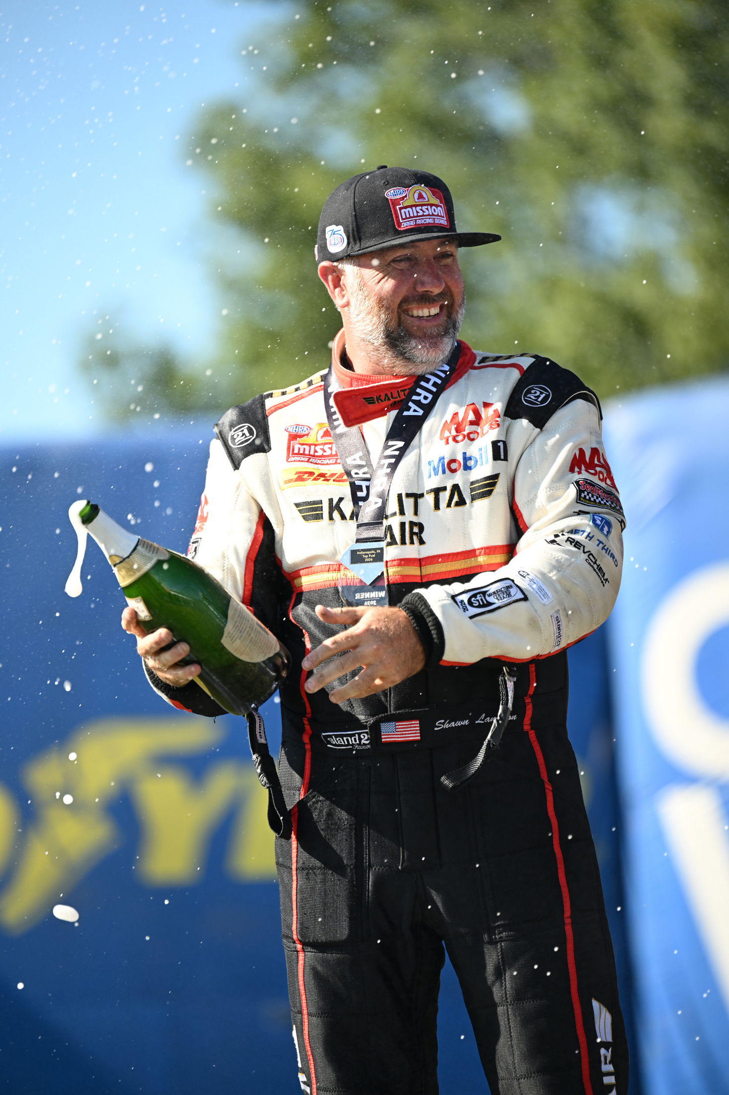 Shawn Langdon holds a champagne bottle in the Kalitta Air firesuit after winning the 2026 NHRA U.S. Nationals