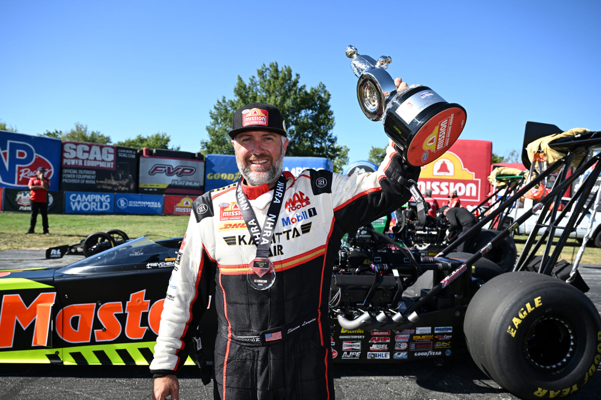 Shawn Langdon raises the Wally trophy beside his Kalitta Motorsports Top Fuel dragster at Indianapolis