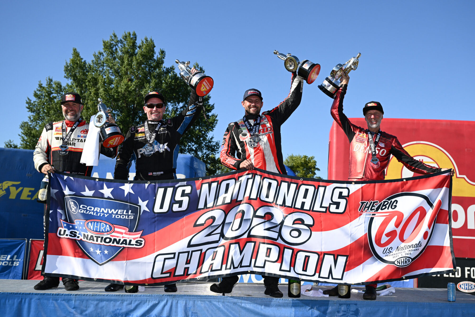 Shawn Langdon, Jack Beckman, Dallas Glenn and Matt Smith hold the U.S. Nationals 2026 Champion banner with their Wallys at Lucas Oil Indianapolis Raceway Park