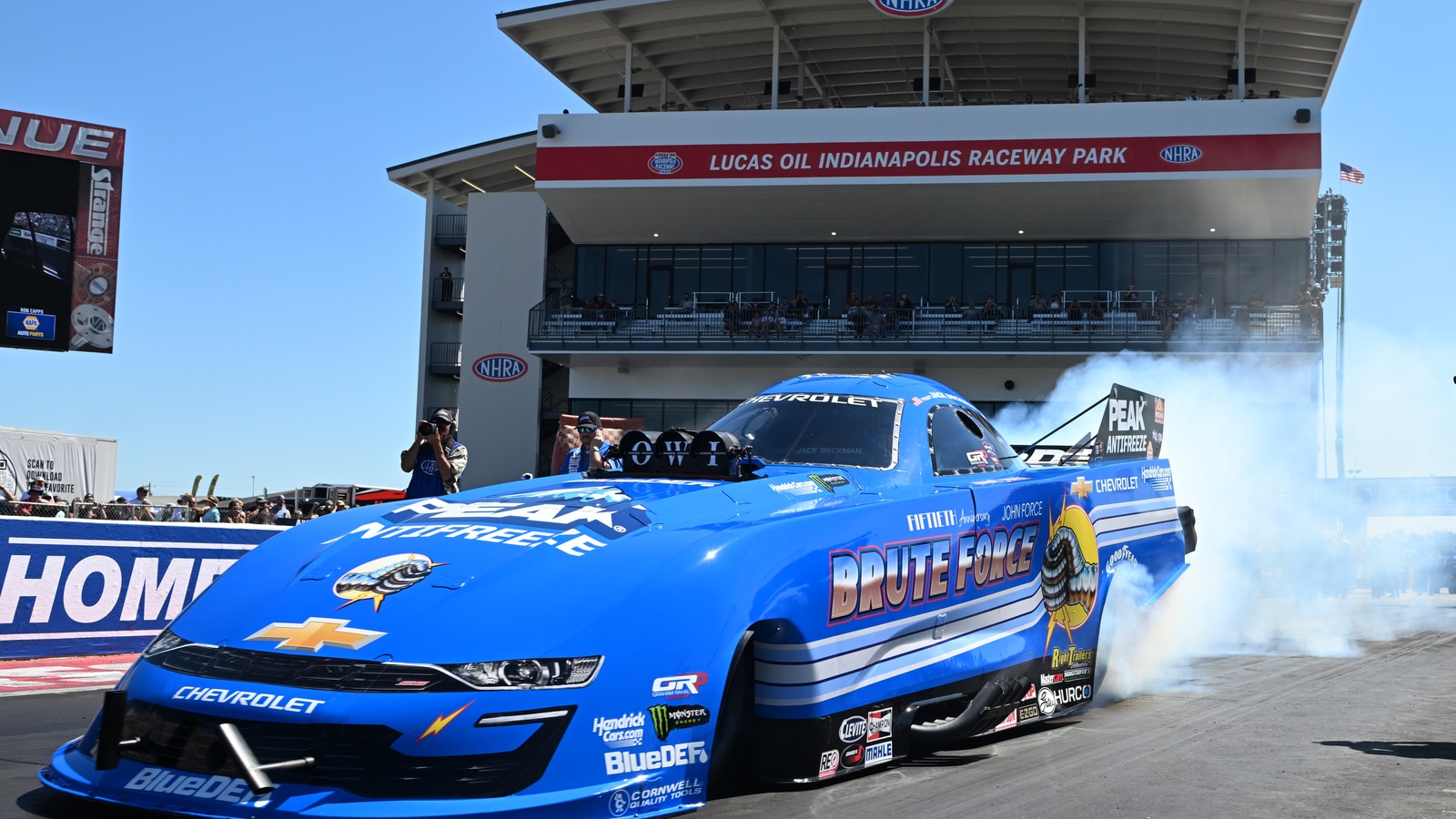 Jack Beckman does a burnout in the blue PEAK Antifreeze Brute Force tribute Funny Car in front of the tower at Lucas Oil Indianapolis Raceway Park