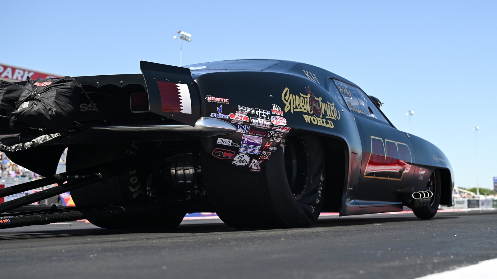 Low angle view of Mike Stavrinos black and red Pro Mod on the starting line at Lucas Oil Indianapolis Raceway Park, Qatar flag on the wing