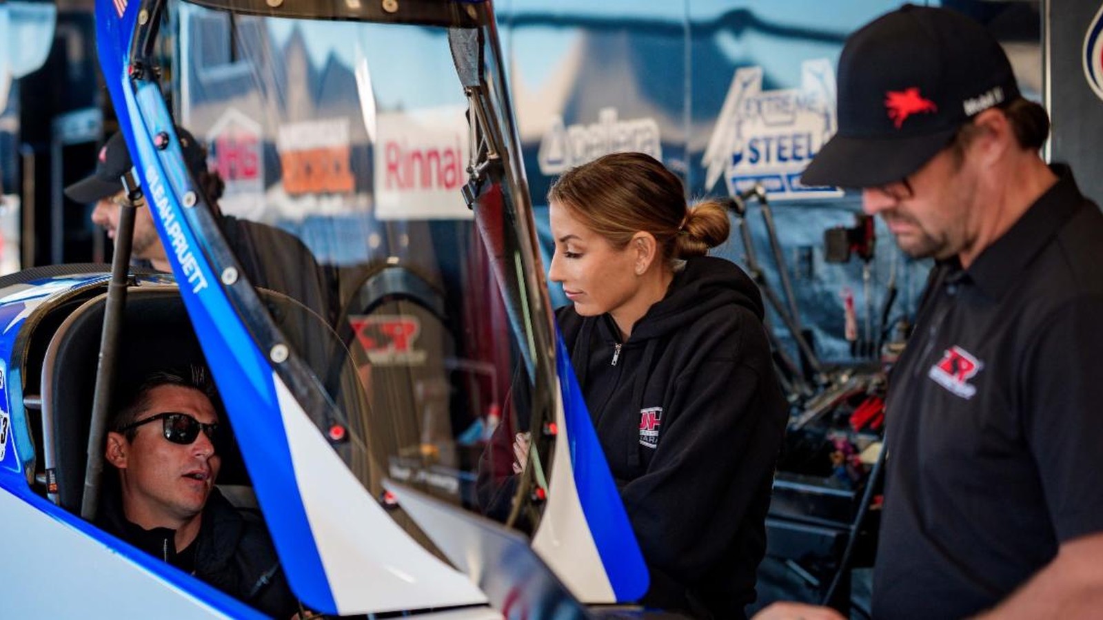 Aaron Stanfield sits in Leah Pruett's Tony Stewart Racing Top Fuel dragster as Pruett looks on at Texas Motorplex